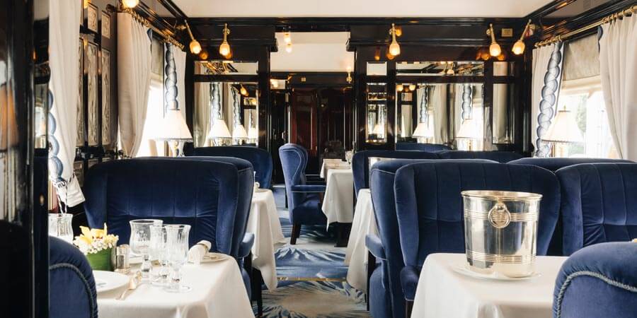 The restaurant car of the Venice Simplon-Orient-Express is decorated with rich blue velvet chairs and neatly presented tables. 